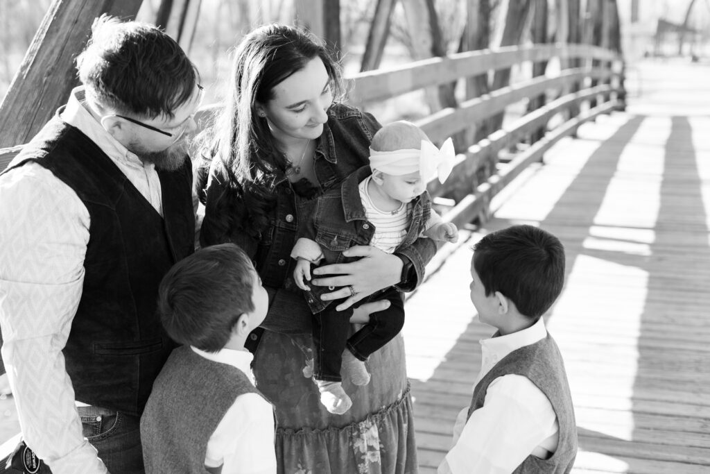 Family stands on bridge at City park smiling at the baby