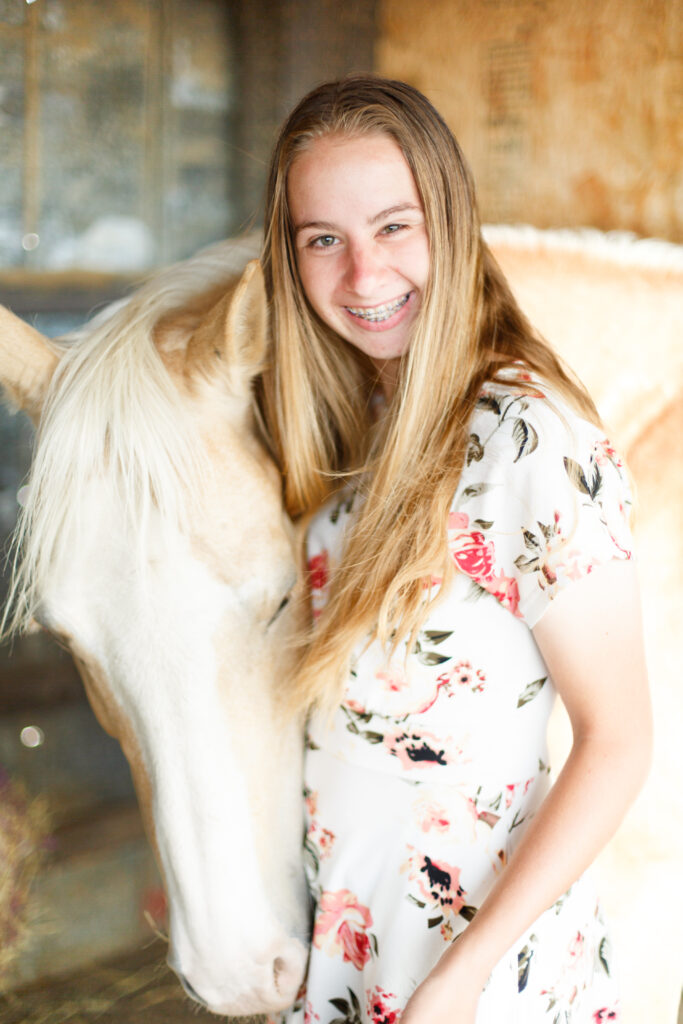 Girl smiles at the camera with horse standing next to her