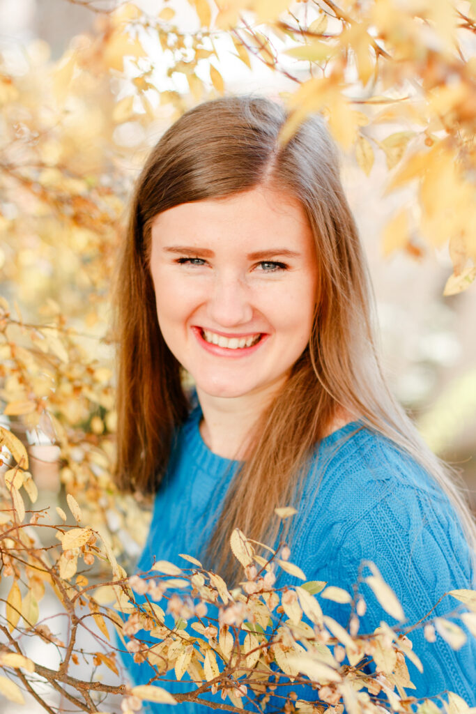 Girl stands in low branches of beautiful yellow tree