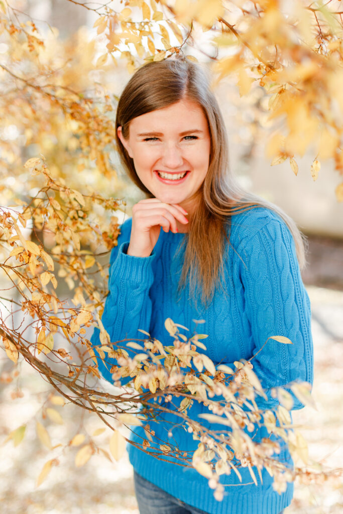 Girl rests head on hand while standing by a beautiful yellow tree