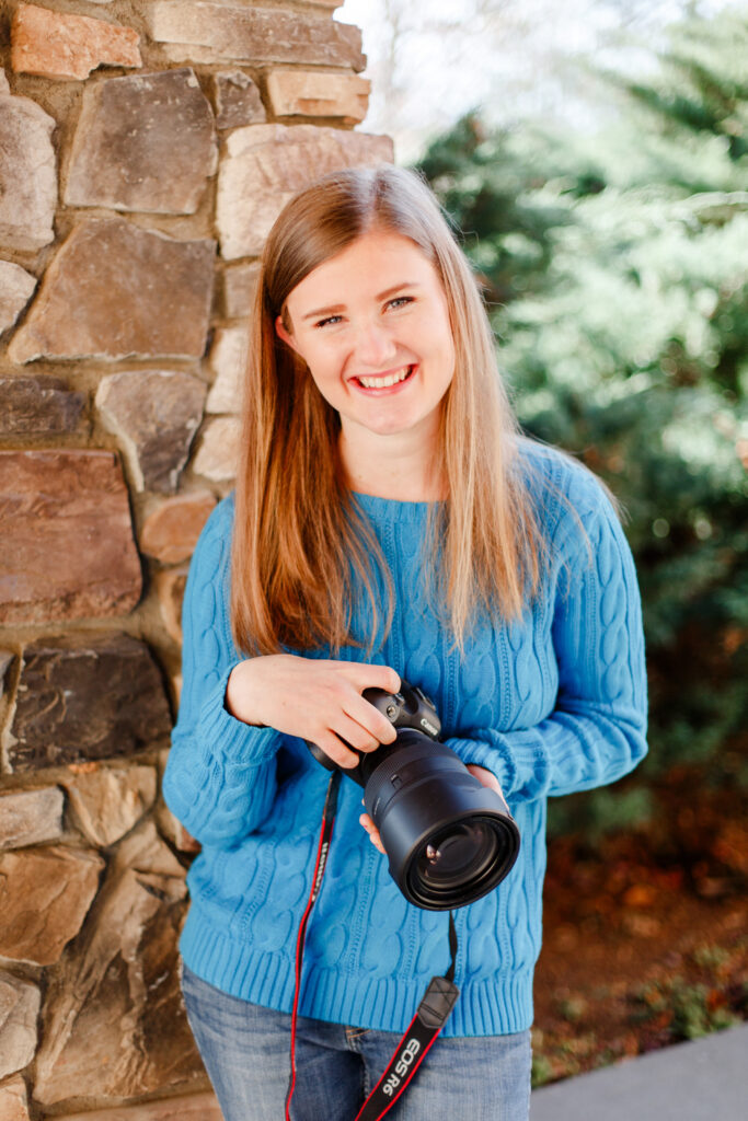 Girl stands by brick wall with her camera