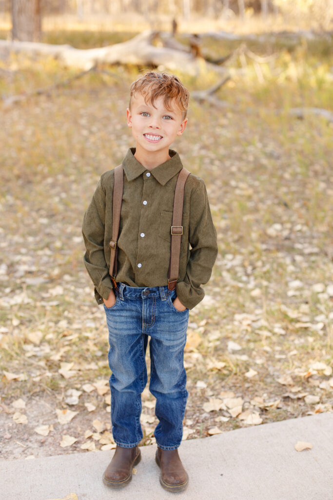 Boy stands with hands in pocket and smiles at fall family session in City Park