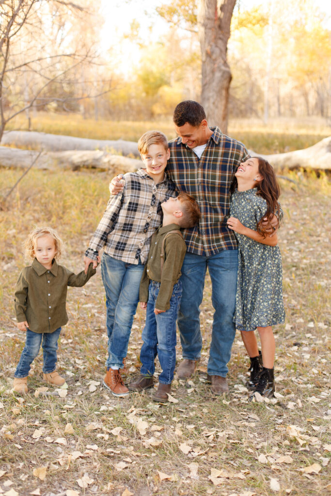 Dad and kids hold hands and laugh together in City Park at fall family session