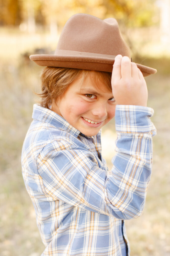 Boy holds brim of hat and smiles in City Park