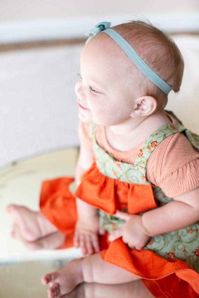 Baby smiles to the side while sitting on a mirror