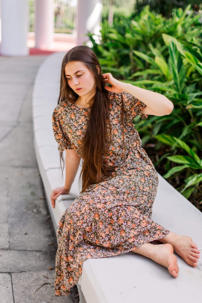 Girl leans on low wall during scenic portrait session in Orlando Florida.