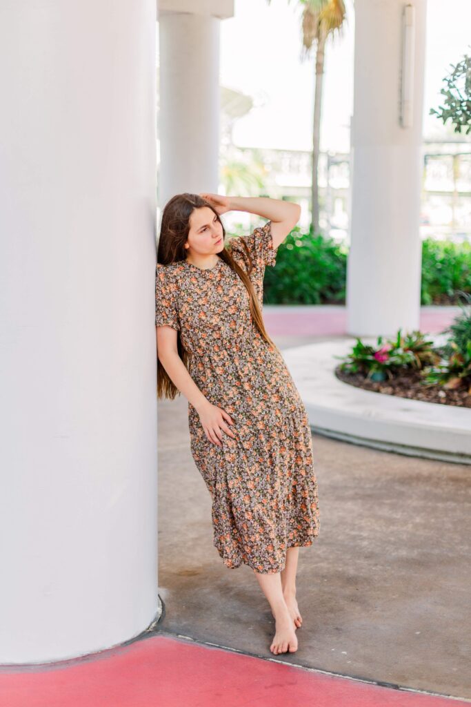 Girl leans against a pillar while tucking her hair behind her ear.