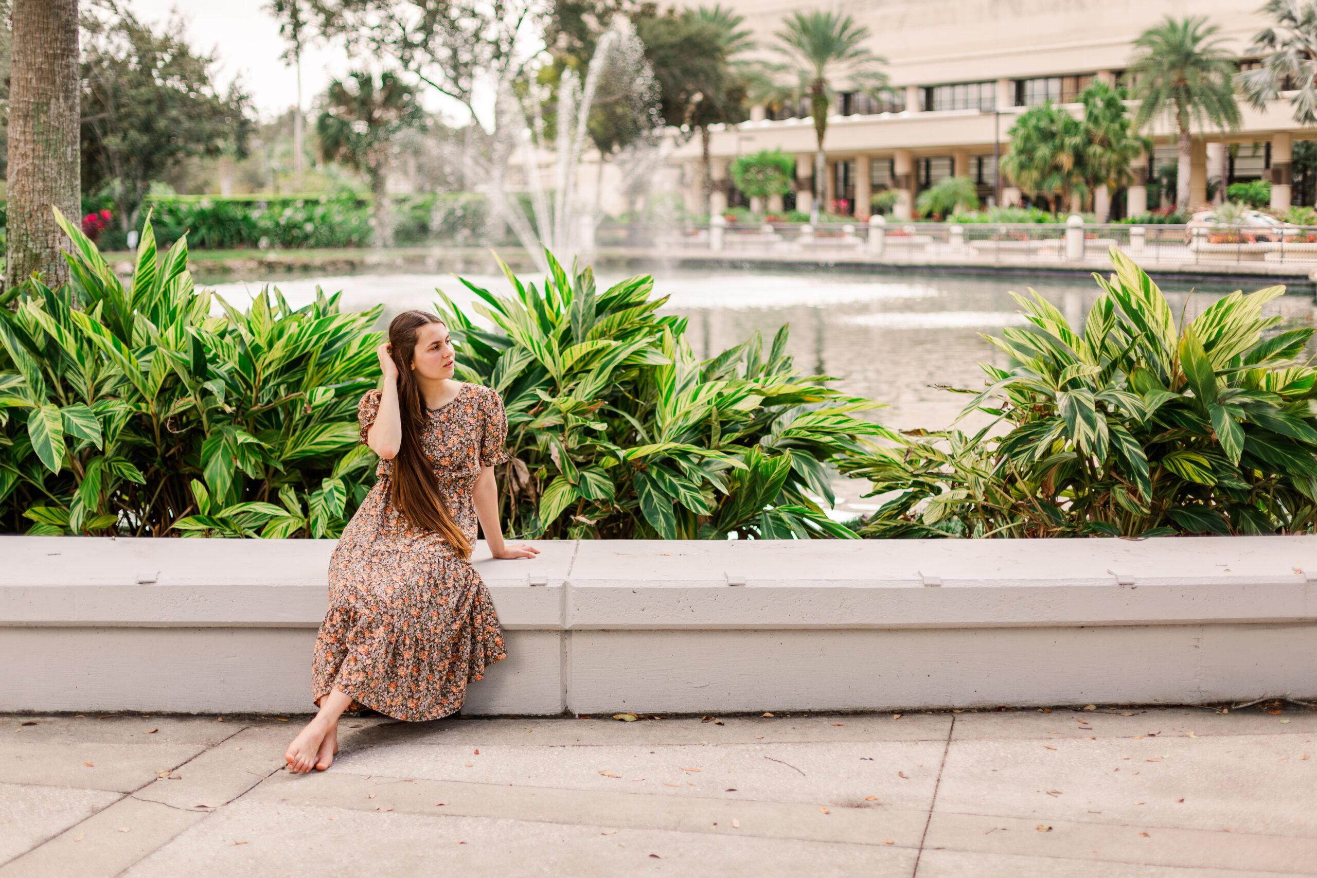 Girl sits on wall and tucks hair behind her ear.