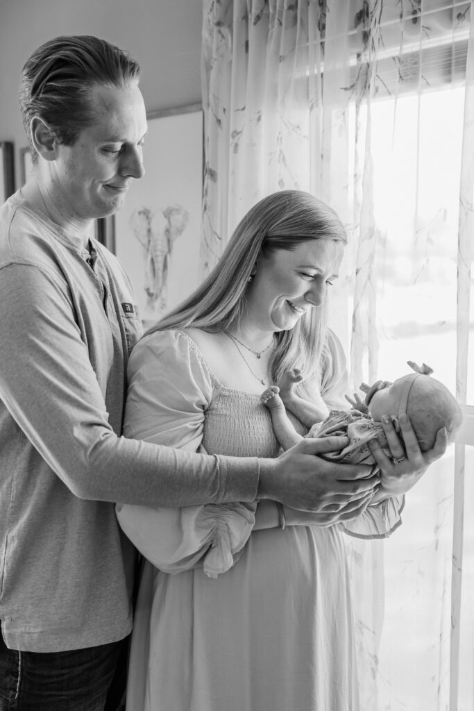Mom and Dad hold baby by the window.