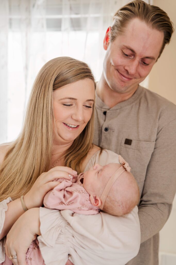 Mom holds baby while Dad smiles down at her during in home newborn session in Pueblo Colorado.