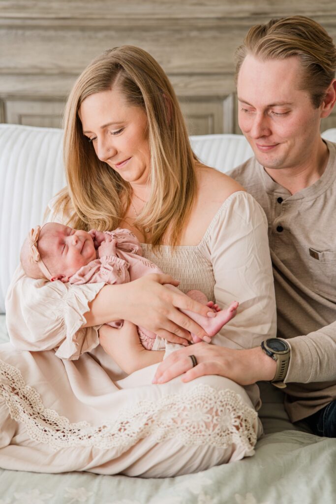Mom holds baby and Dad smiles at them during lifestyle newborn session