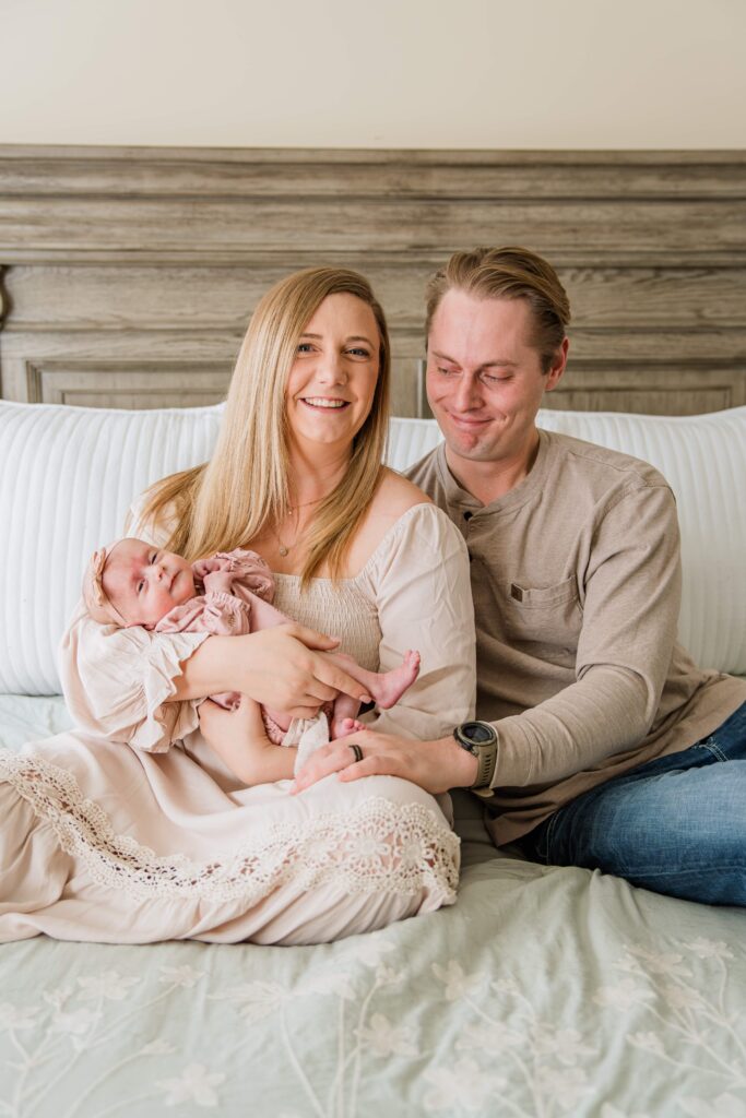 Mom holds baby and laughs towards the camera while dad smiles down at his daughter.
