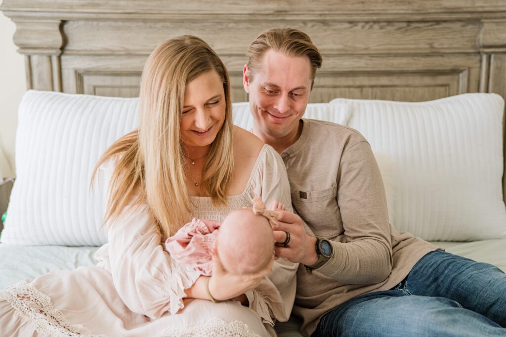 Dad and Mom talk and smile at their infant daughter during lifestyle newborn session in Pueblo Colorado