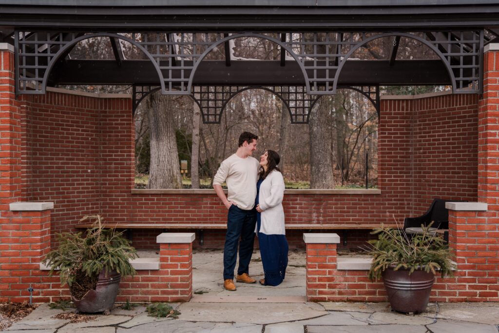 Couple stands under an arbor at a snowy maternity session at Kingwood Center Gardens, Mansfield, OH