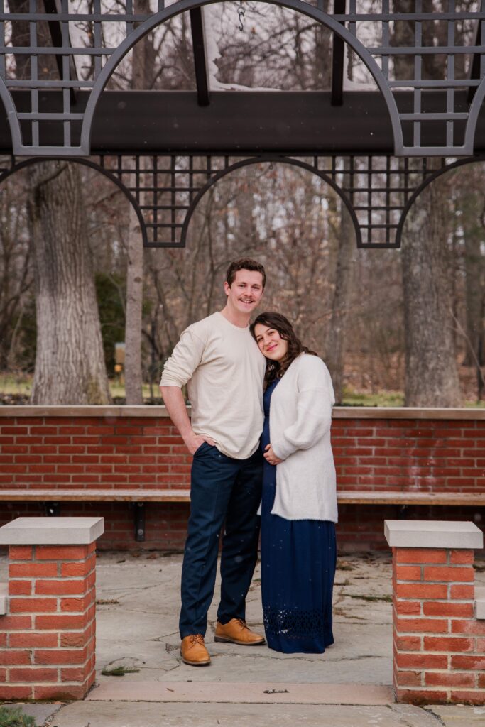 Couple smiles at camera under an arbor.