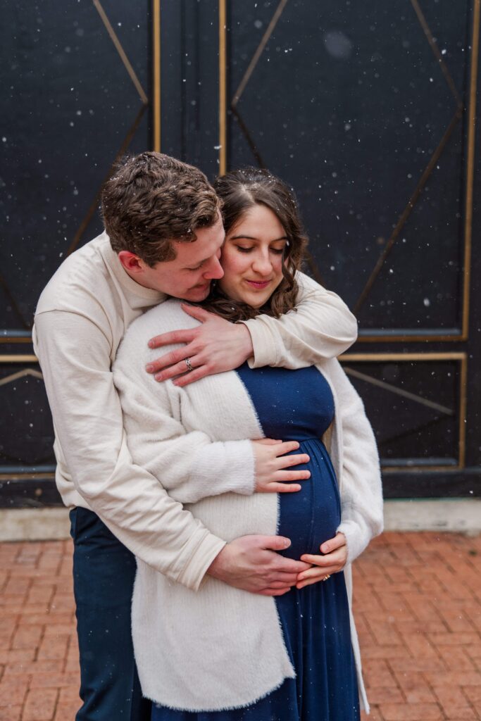Husband and wife rest their hands on baby bump and look down.