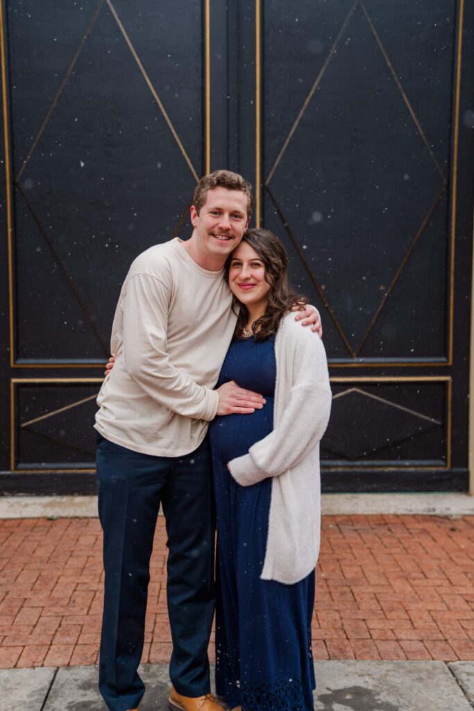 Husband and wife rest their hands on baby bump. and smile at each other.