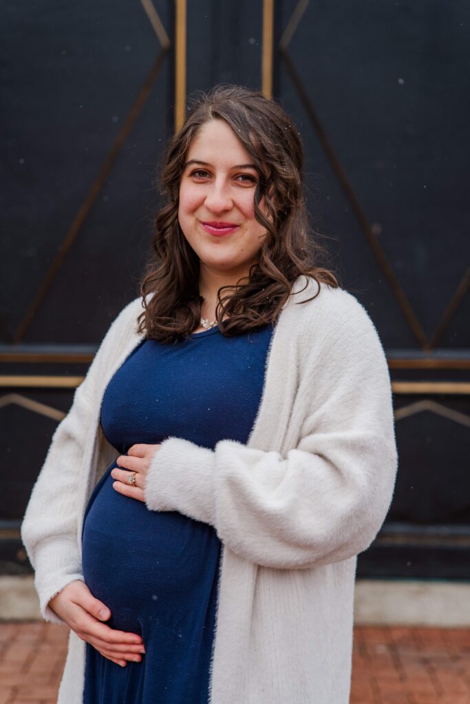 Mother smiles at camera with hands on baby bump.