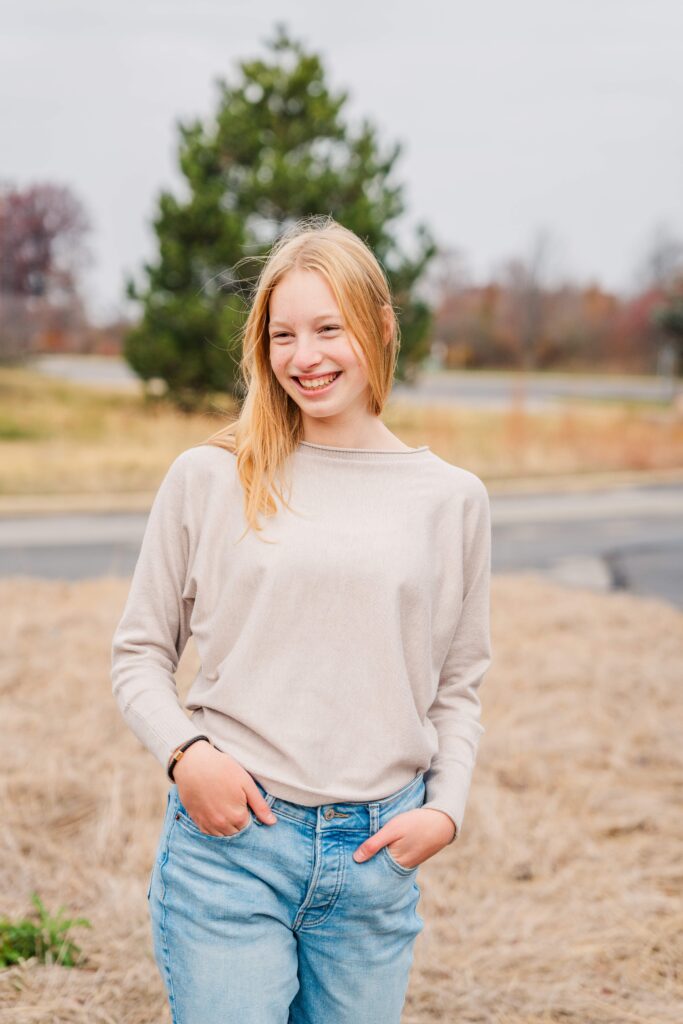 Girl smiles at the side with her hands in pockets