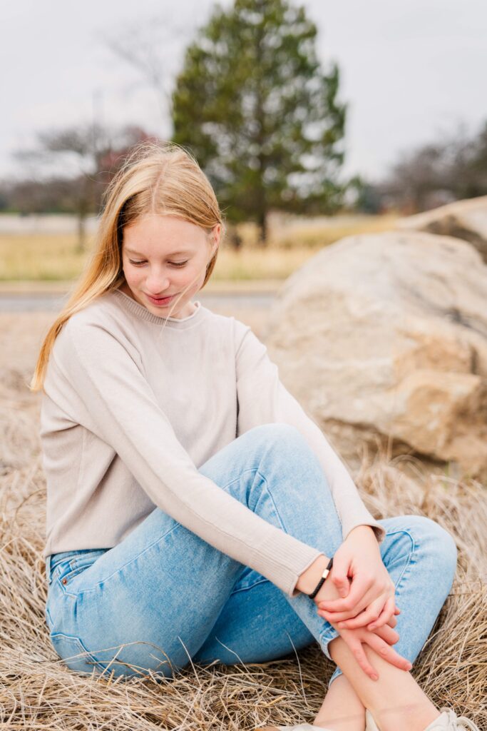 Girl looks down while sitting during cloudy winter portrait session.