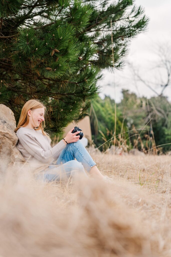 A girl smiles down at her camera while sitting against a rock during a cloudy winter portrait session in Sandusky, Ohio.