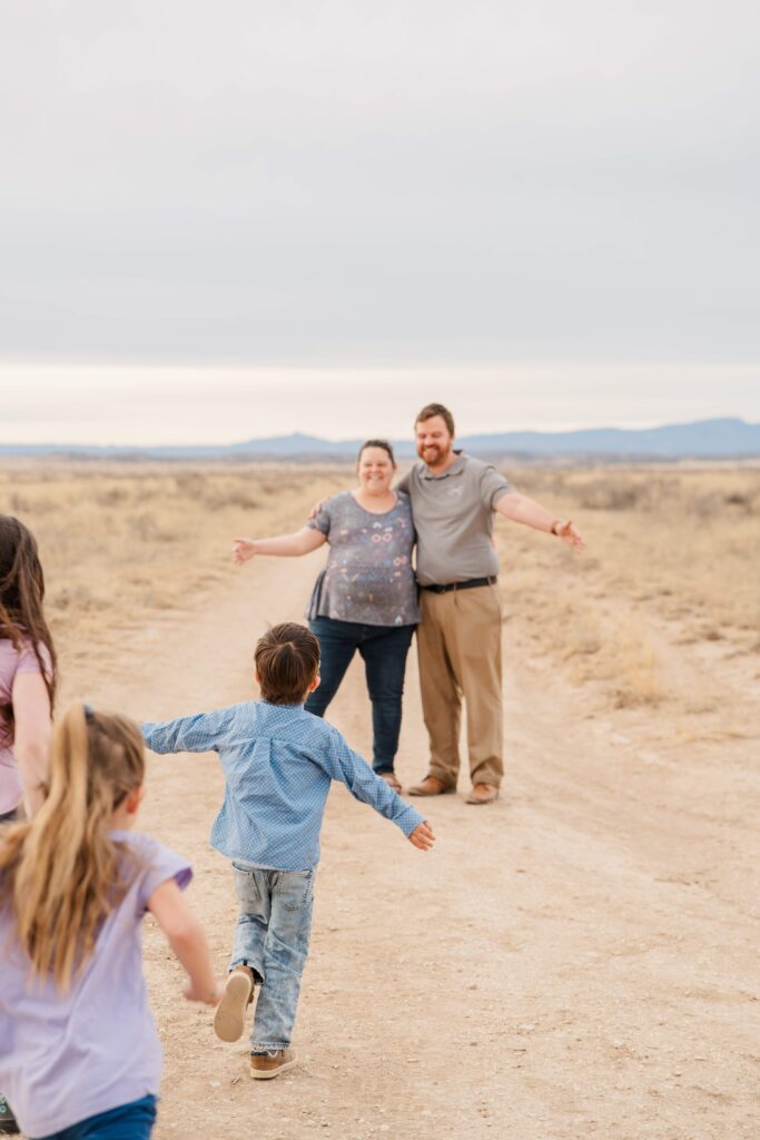 Dad and Mom hold out their arms, and son runs to them with his arms held out.