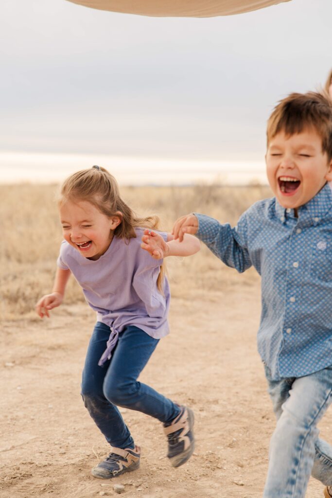 Two of the kids run under the blanket while laughing.