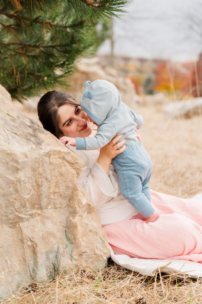 Mom leans against a rock and holds baby upright in her lap.