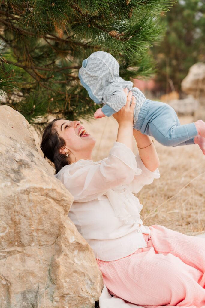 Mama laughs while holding her baby up in the air.