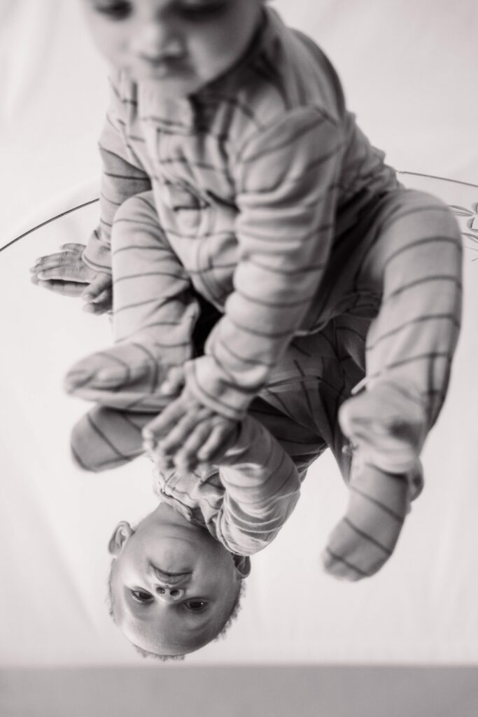 Black and white of baby sitting on a mirror